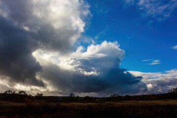 Massive, dramatic storm clouds dominate a vibrant blue sky. Light bursts through, casting an ethereal glow over a serene autumn field