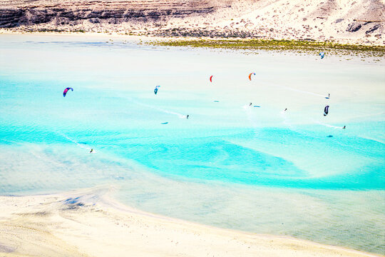 Aerial view of kite surfers dancing across the turquoise waters, contrasting against the arid landscape, Parco natural de Jandia, Costa Calma, Fuerteventura, Canary Islands, Spain.