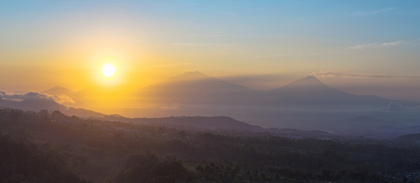 Aerial view of a radiant sunrise casting a golden glow over misty mountains and lush hills, volcano Merapi, Java, Indonesia.