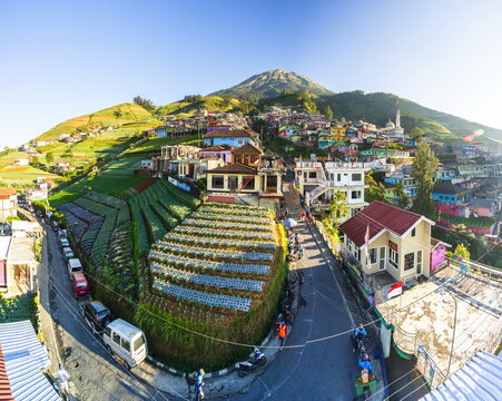 Aerial view of vibrant homes nestled against the mountain's green slopes beneath a bright blue sky, Nepal Van Java, Java, Indonesia.