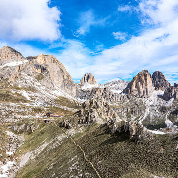 Aerial view of rugged, snow-dusted peaks under a vibrant sky, where sharp rocks meet soft grass in a stunning display of nature's artistry. Roda de Vael, Fassa valley, Trentino-South Tyrol, Italy.