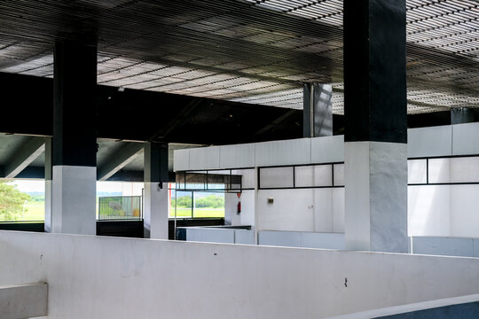 Modern building showcases empty white commercial partition stalls, large columns, and an open layout revealing lush green outdoor landscapes through windows.