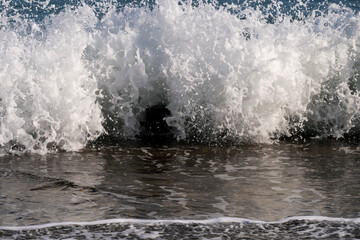 a powerful wave crashing onto the shore, exploding into a wall of white foam and spray over dark wet sand.