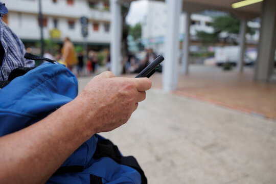 mano di uomo adulto che regge e usa un telefono, mentre sta seduto all'aperto, di giorno, in estate, in un luogo pubblico