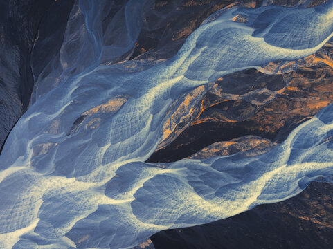 Aerial view of glacial rivers weaving intricate patterns across the volcanic landscape, a tapestry of icy blues and earthy browns, Skogar, Iceland.