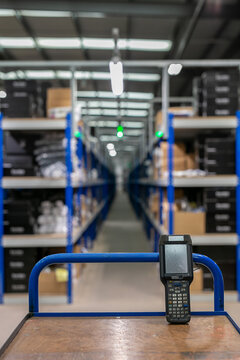 Interior of a logistics warehouse with multi-tier shelving and pallet racking, showing a handheld barcode scanner on a picking trolley used for order picking and inventory management