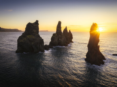 Aerial view of basalt sea stacks rise majestically from the turbulent Atlantic, illuminated by the golden glow of the setting sun near Reynisfjara Beach, Vik I Myrdal, Myrdalshreppur, Iceland.