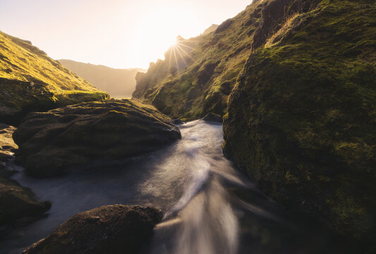 View of a serene river flowing between moss-covered cliffs under a radiant sun in the Icelandic highlands, Sudurland, Iceland.