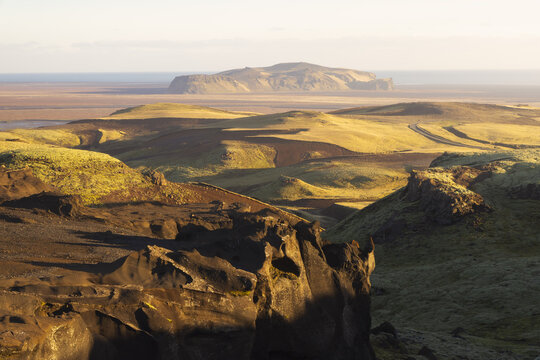 View of a rugged landscape under a warm glow with distant landforms and shadowed foreground rocks, Sudurland, Myrdalshreppur, Iceland.