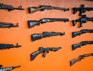 Diverse collection of historical and modern firearms, rifles, and shotguns displayed on an orange...
