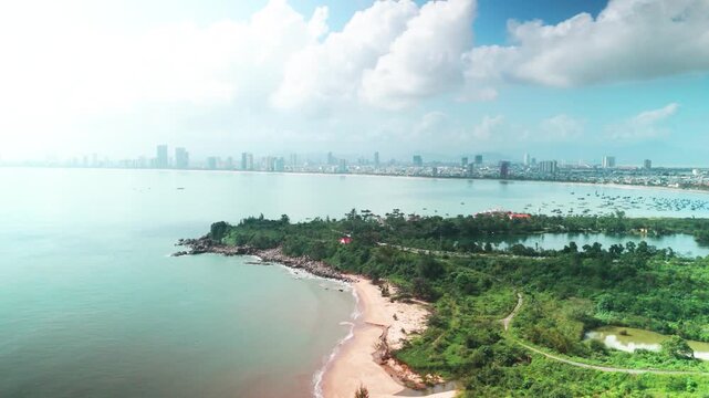 Da nang city skyline stretching along the coastline with son tra peninsula in foreground, showing sandy beaches, lush greenery, and the bay filled with fishing boats under a bright sky