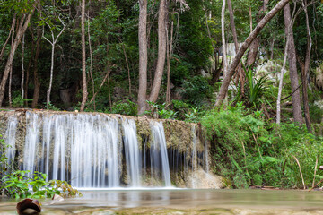 Cascading Erawan Falls in Erawan National Park, Thailand. Lush green forest surrounds the flowing water. Tropical trees and plants frame the scenic waterfall setting.