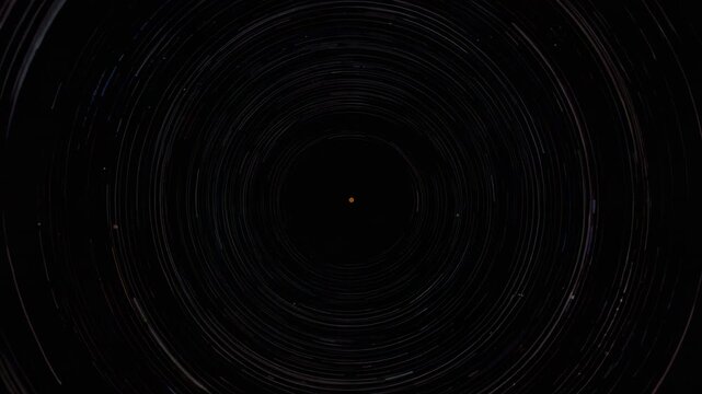 Starting timelapse camera capturing rotation of concentric star trails in polar sky, orange dot