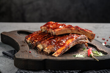 Sticky BBQ pork ribs glazed with sweet and spicy sauce on wooden serving board. Tender grilled spare ribs with rosemary and chili pepper garnish, delicious comfort food meal.