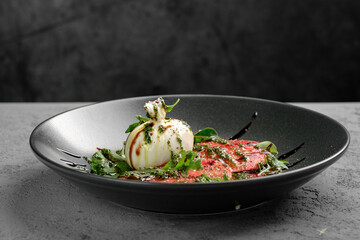Fresh tomato carpaccio with creamy burrata, pesto drizzle, fresh basil leaves and balsamic glaze on black plate. Elegant Italian appetizer, gourmet salad-style dish, restaurant presentation