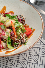 Asian-inspired salad with glazed teriyaki beef chunks in sesame seeds, fresh mixed greens, cherry tomatoes, carrot strips and soy dressing in rustic white bowl. Vibrant fusion gourmet dish