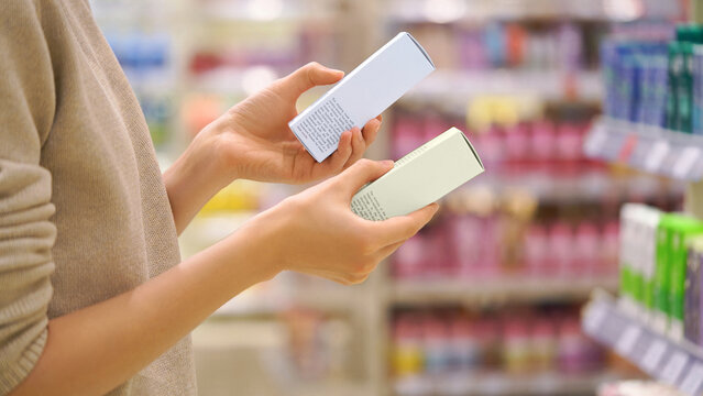 Customer Reading the Ingredient Labels Compares Two Skincare Products in Beauty Store. Close-up of a Female Hands, Woman Choosing Cosmetic Product. Makeup Selection. Conscious Choice. Mindful Shopping