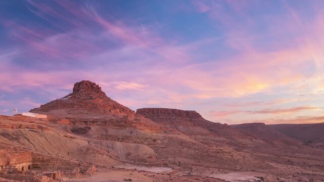Timelapse: Ksar Guermassa hilltop berber village at sunset, rocky desert landscape dramatic sky, ancient architecture, arid terrain, heritage, history, travel destination, Tataouine, Tunisia