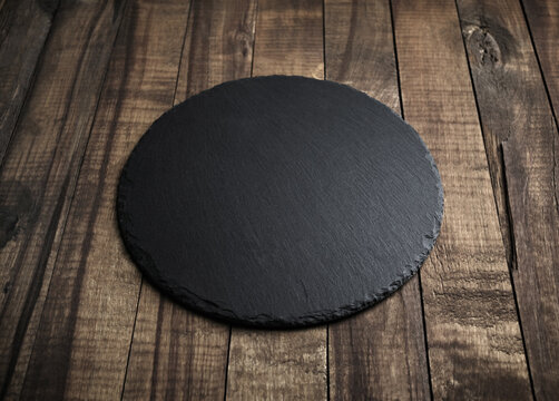 Blank black round slate plate on wooden surface. Copy space.