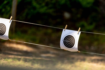Paper rifle targets labeled "official rifle target" hang from a rope line at an outdoor shooting range, secured with clips and ready for practice sessions.