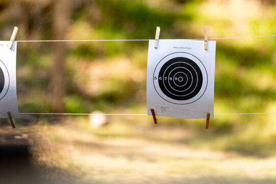 Paper rifle targets labeled "official rifle target" hang from a rope line at an outdoor shooting range, secured with clips and ready for practice sessions in a straightforward range setup.