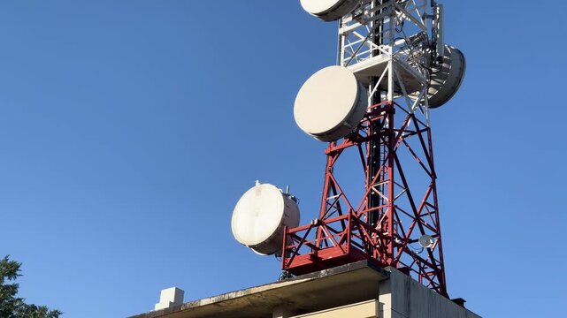 Tall telecommunications tower with numerous antennas and satellite dishes on its roof against clear blue sky. Satellite, cellular, or microwave communications.