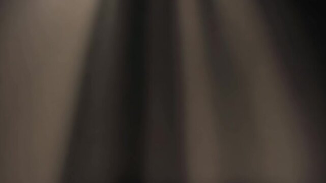 Subtle abstract background featuring warm vertical light rays filtering gently through dark moody shadows creating a dramatic atmospheric cinematic visual effect