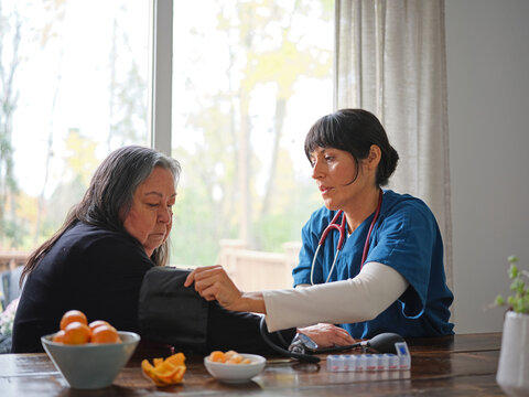 Native American nurse fits blood pressure cuff on elder woman's arm at table