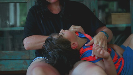 Child lying on back with head on mother&rsquo;s lap, looking up as mother caresses hair in calm domestic scene filled with tenderness, trust, and intimacy