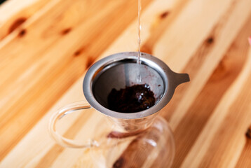 Thin stream of hot water pours into metal filter with ground coffee in Chemex. Alternative brewing...