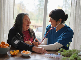 Native American nurse smiles while taking patient's blood pressure at table