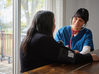 Native American nurse checks blood pressure at table of elderly patient