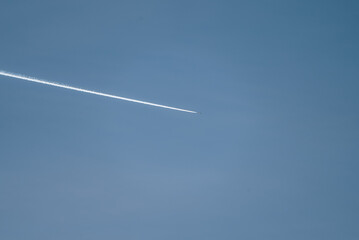 Airplane traversing a clear blue sky at high altitude, a visible long white condensation trail following behind, representing international travel, aviation, and the concepts of flight and freedom