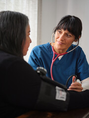 Native American nurse watches elderly patient while checking blood pressure