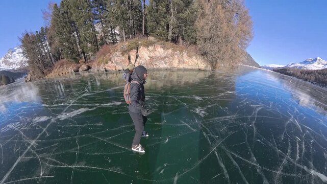 Couple skating on transparent black ice at frozen Lake Sils in the Swiss Alps