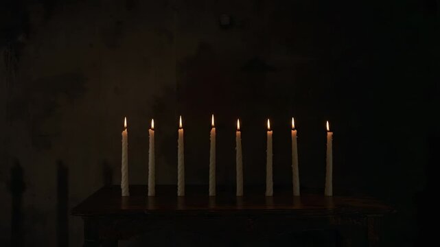 Flickering nine taper candles shifting height on wood table with holders indoors from soft breeze