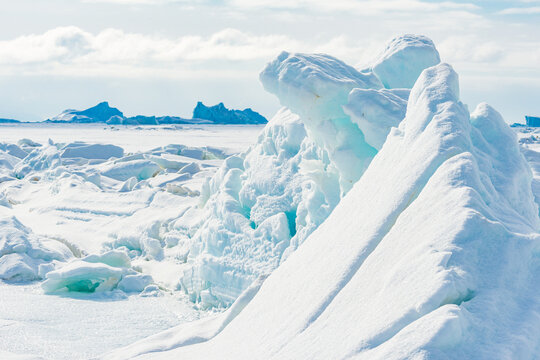 Ice formations on frozen sea near Qaanaaq village in Greenland with distant mountains and cloudy sky