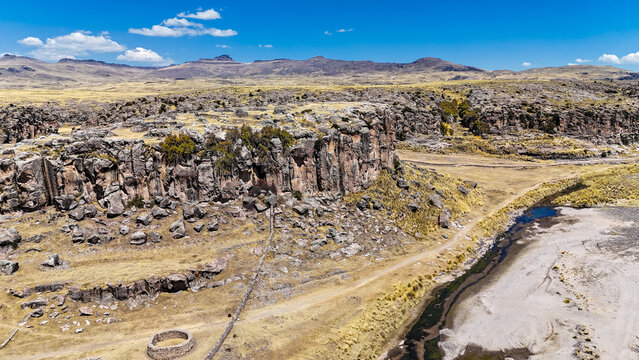 Aerial view of rugged cliffs dropping to a winding river cutting through the arid landscape, a testament to time's relentless artistry, Espinar, Cusco, Peru.