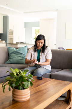 Woman sitting on grey sectional sofa in modern living room manipulating small medication bottle
