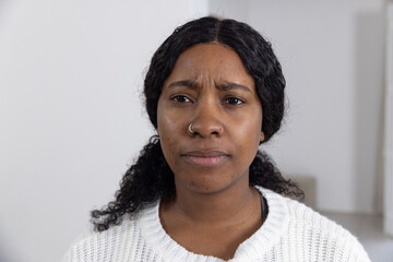 African American woman wearing white sweater, dark top, hoop nose ring, showing concern in room