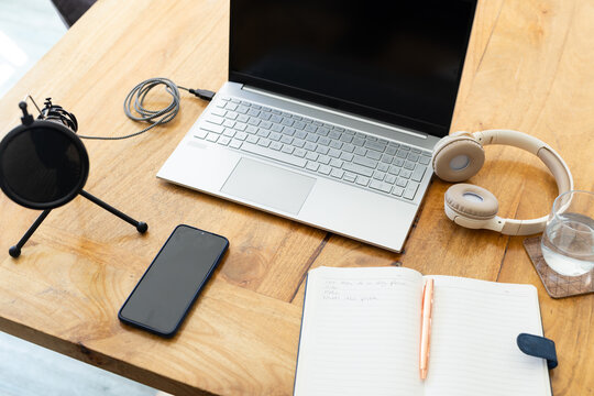 Silver laptop sitting open on wooden desk, catching sunlight, with headphones and mic nearby