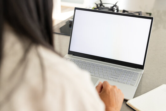 Silver laptop is sitting open on gray countertop near window, notebook and gas stovetop visible