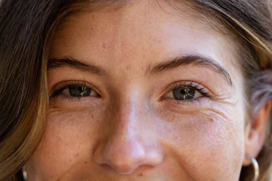 Woman showing freckled skin and crow's feet while gazing in close-up portrait with hoop earring