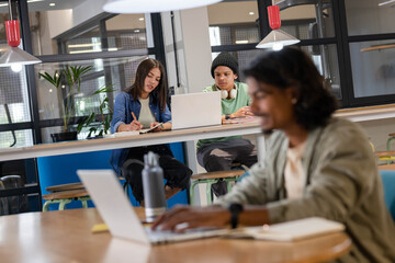 Diverse coworkers working in modern coworking space around laptops and notebooks, copy space