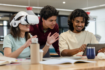 Colleagues with female wearing white VR headset while male using tablet and notebooks on table