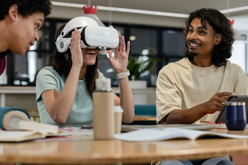 Coworkers collaborating around table in study area, woman adjusting VR headset, man holding tablet