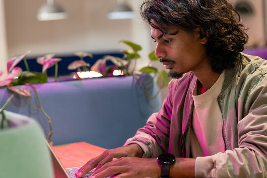 African man typing on laptop at modern lounge, wearing light jacket and smartwatch