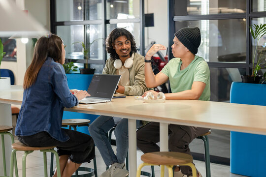 African American coworkers sitting and discussing at long table in coworking space with laptop