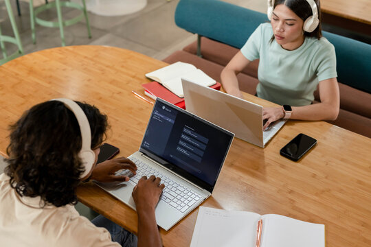 African American peers wearing white headphones, woman in mint-green top, typing on laptops in cafe
