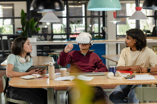 African team watching male wearing white VR headset gesturing at table in office with tablet laptop - Powered by Adobe